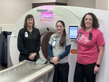 Picture of three female radiology techs, standing in front of a MRI machine.