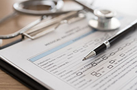 Clipboard is sitting on top of a table with paperwork, a stethoscope, and pen