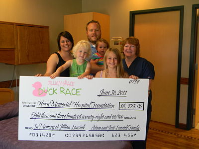 Female Nurse is standing next to a family and their three children. They are holding a check that says DUCK RACE.